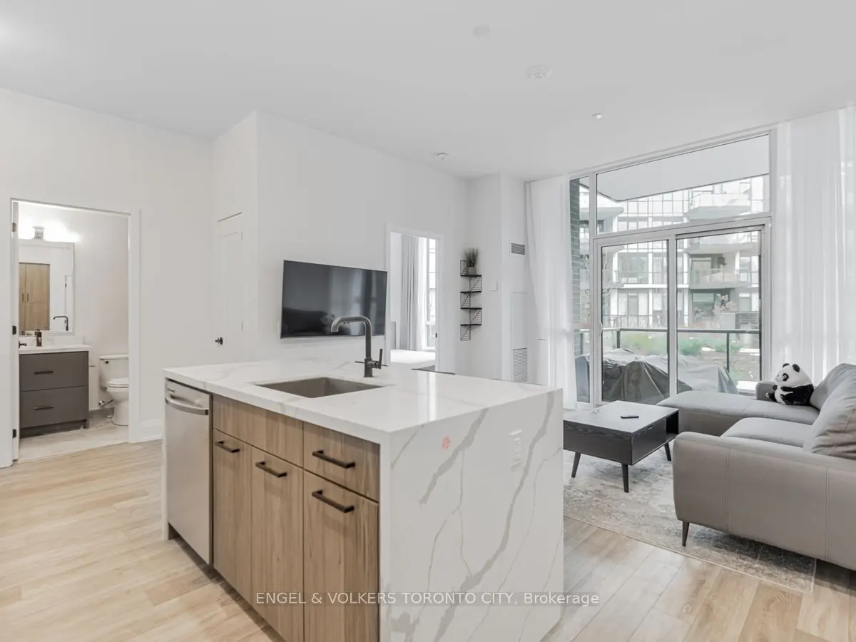Modern open-concept condo with a marble kitchen island, wood cabinets, gray sofa, and balcony view.