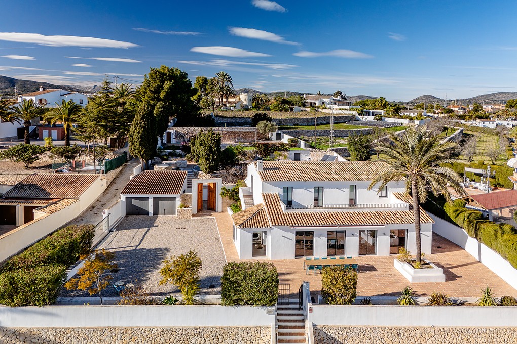 Aerial view of a two-story white house with a terracotta tile roof, a brick patio, and a palm tree in the yard. [AI-generated text]