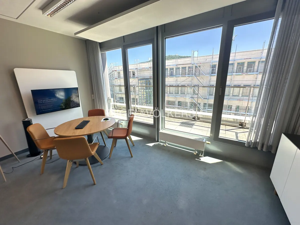 Conference room with an oval table, four chairs, and a large window overlooking a building under construction.
