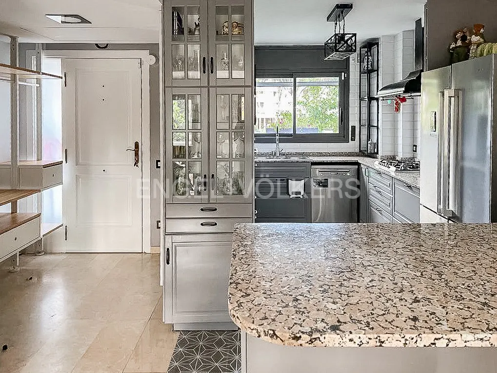 A bright kitchen with gray cabinets, a granite countertop, and stainless steel appliances. A white door is visible on the left.