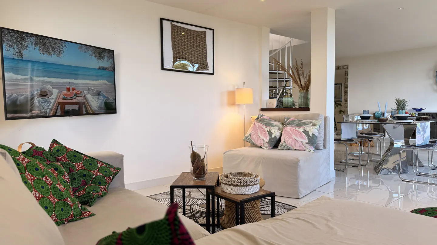Living room with white walls, a sofa with green patterned pillows, and a beach scene picture on the wall.