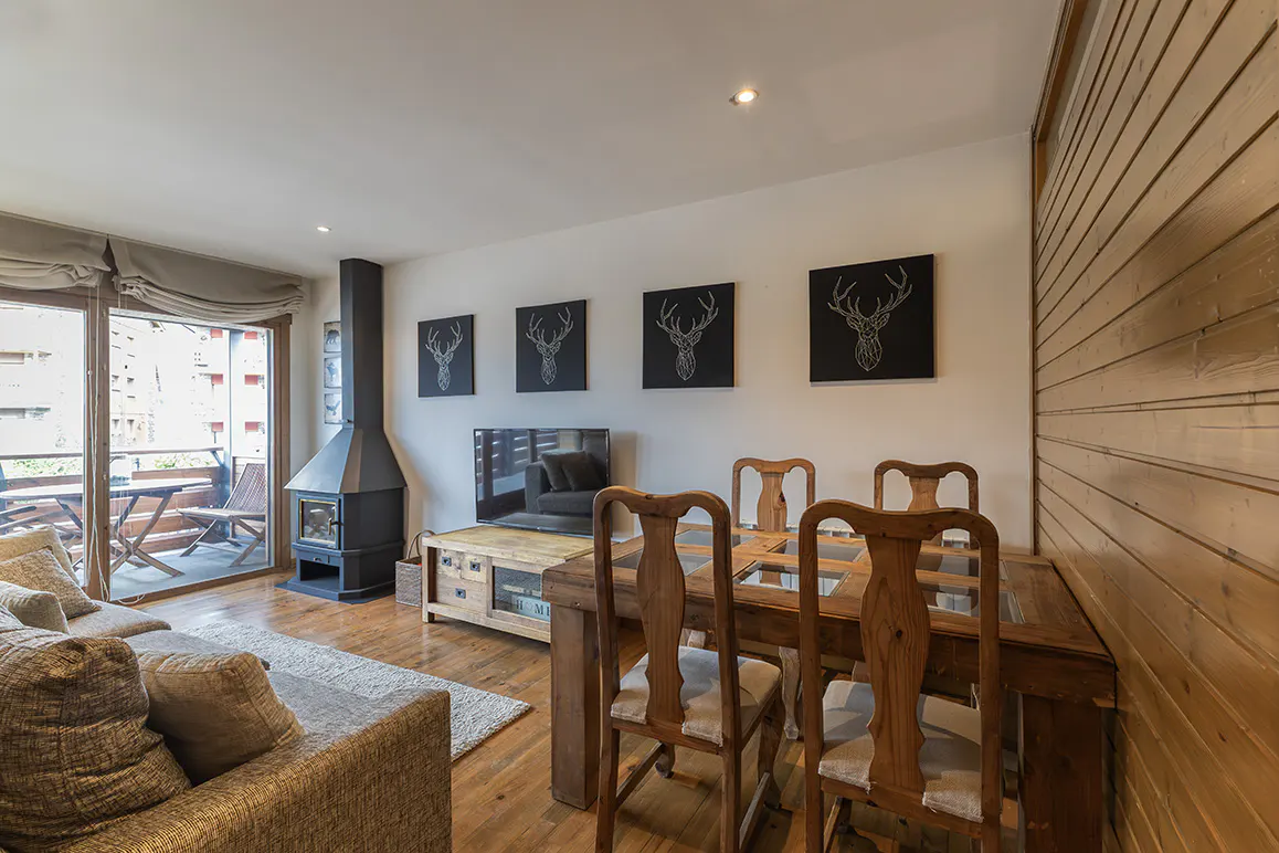 Living room with wood floors, a fireplace, and a dining table with four chairs. Deer artwork hangs on the wall. Balcony with table and chairs.