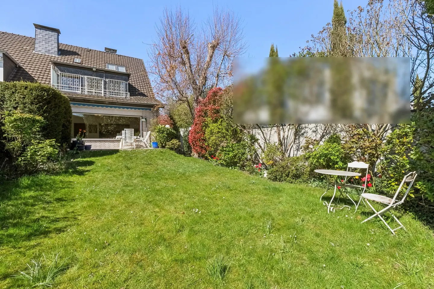 A house with a large green lawn and a white table and chairs set on the right side of the lawn.