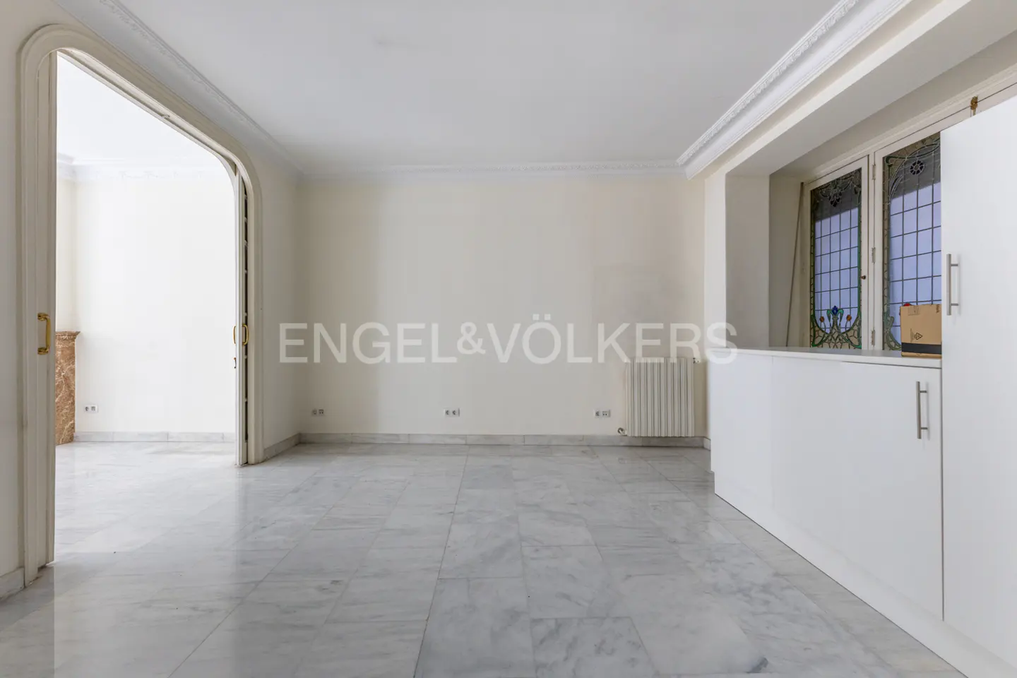 Empty room with marble floors, white walls, and an arched doorway. White cabinets and stained glass windows are on the right.