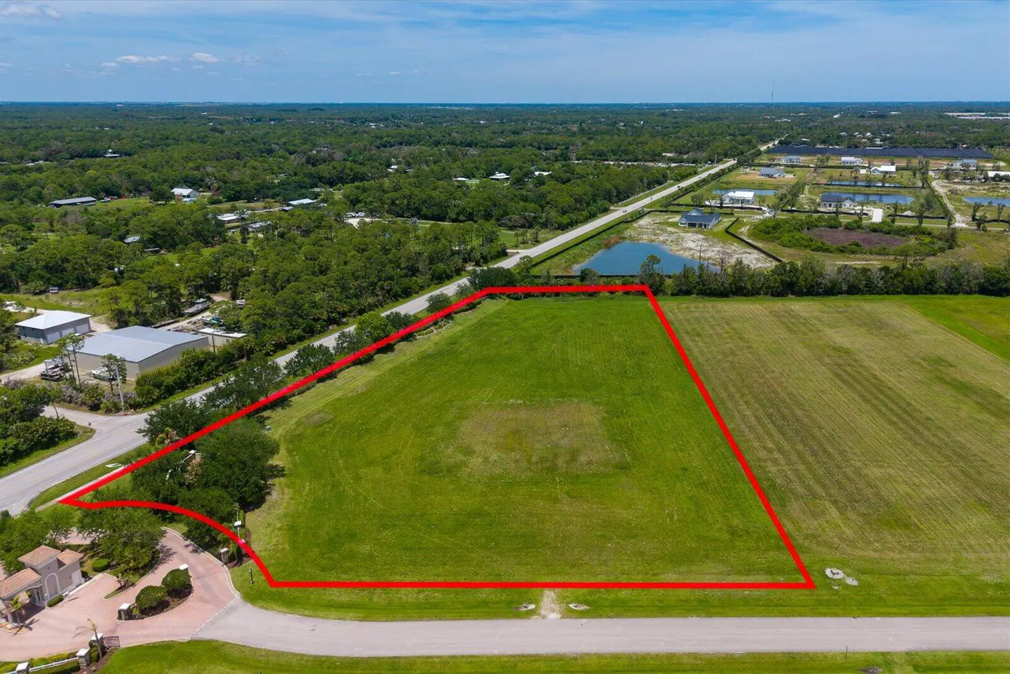 Aerial view of a large, grassy lot outlined in red, ready for development in a green, suburban area.