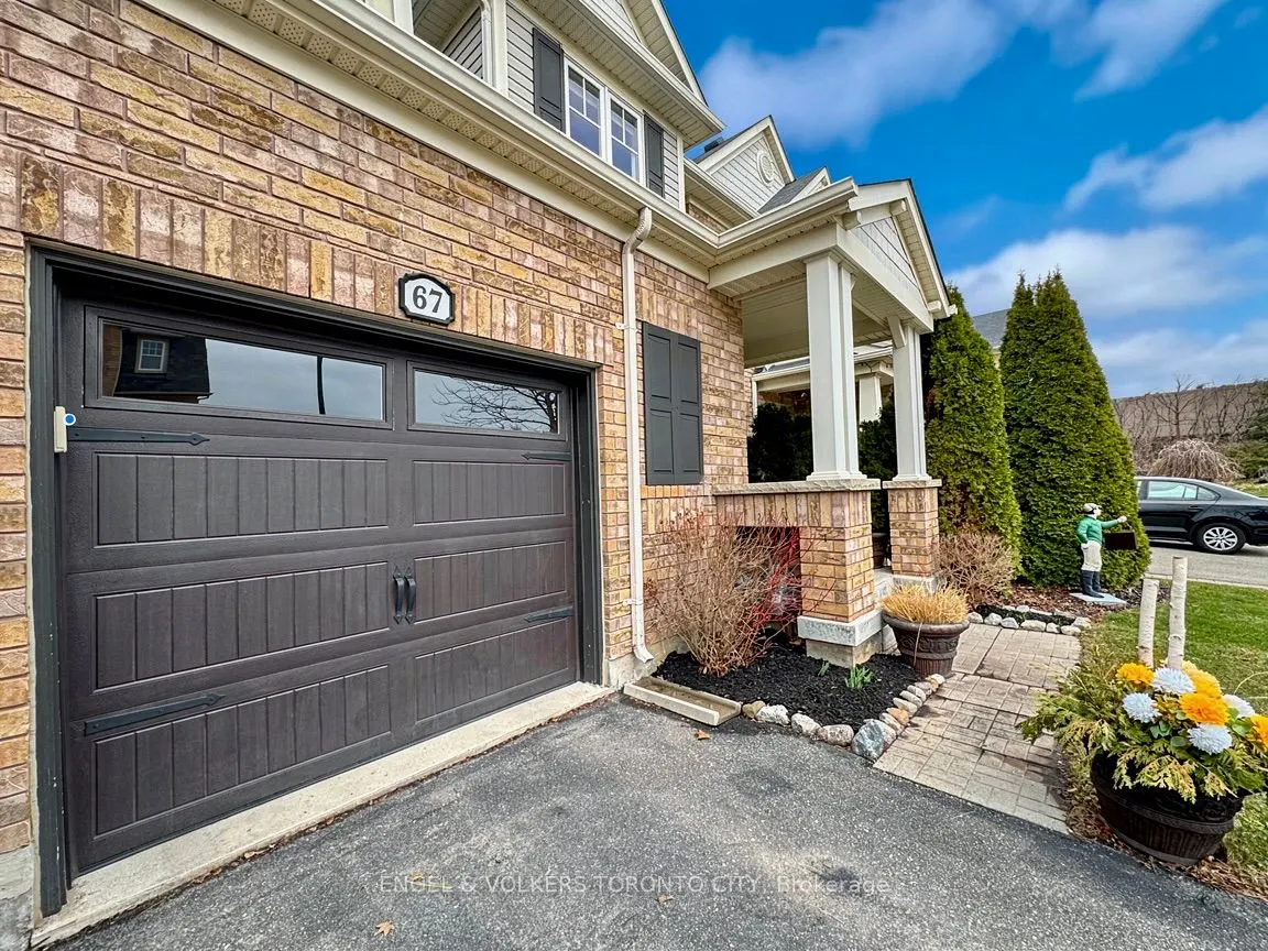Exterior of a brick house with a brown garage door, white pillars, and a green lawn with a statue.