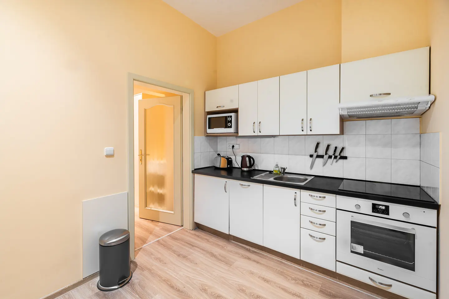 Small kitchen with white cabinets, black countertops, stainless steel appliances, and light yellow walls.