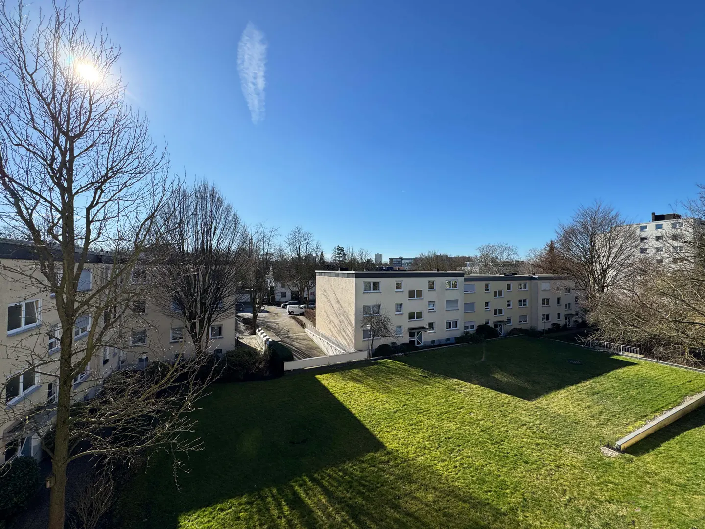 Apartment complex view with green lawn, trees, and blue sky on a sunny day.