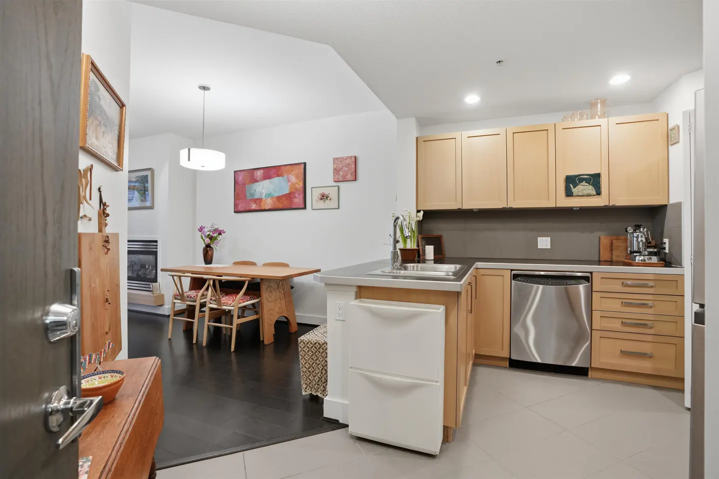 A bright, modern kitchen with light wood cabinets, stainless steel appliances, and a dining area with a wooden table and chairs.