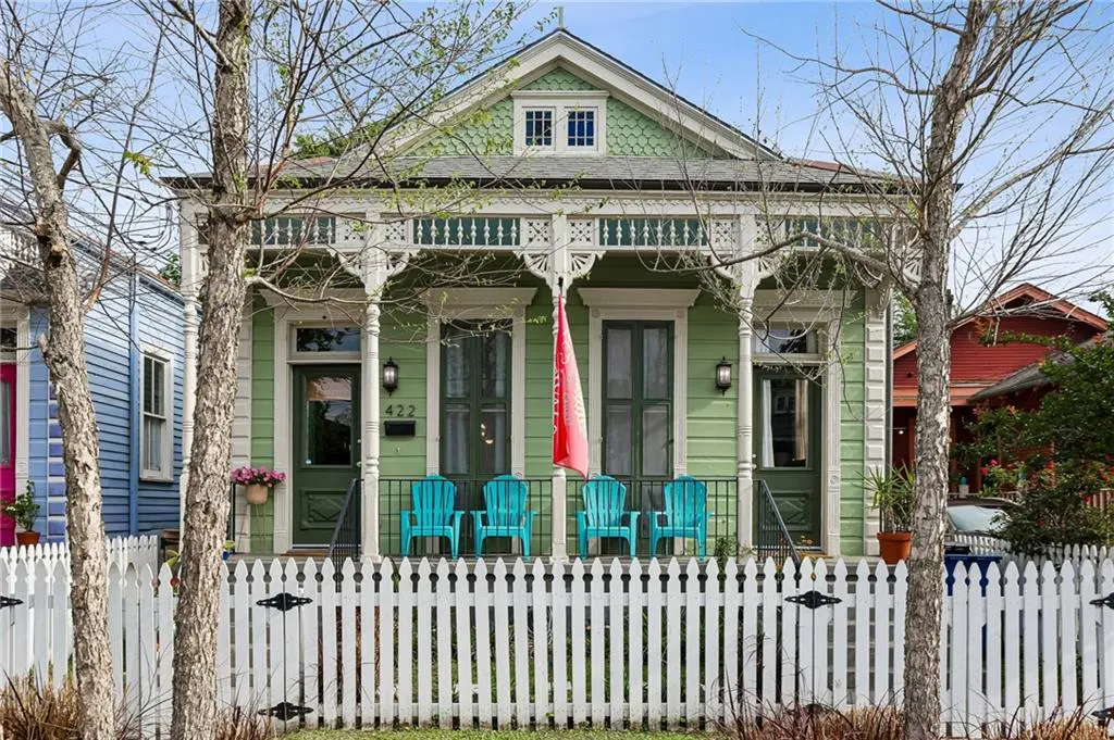 A light green house with a white picket fence and four blue chairs on the porch.