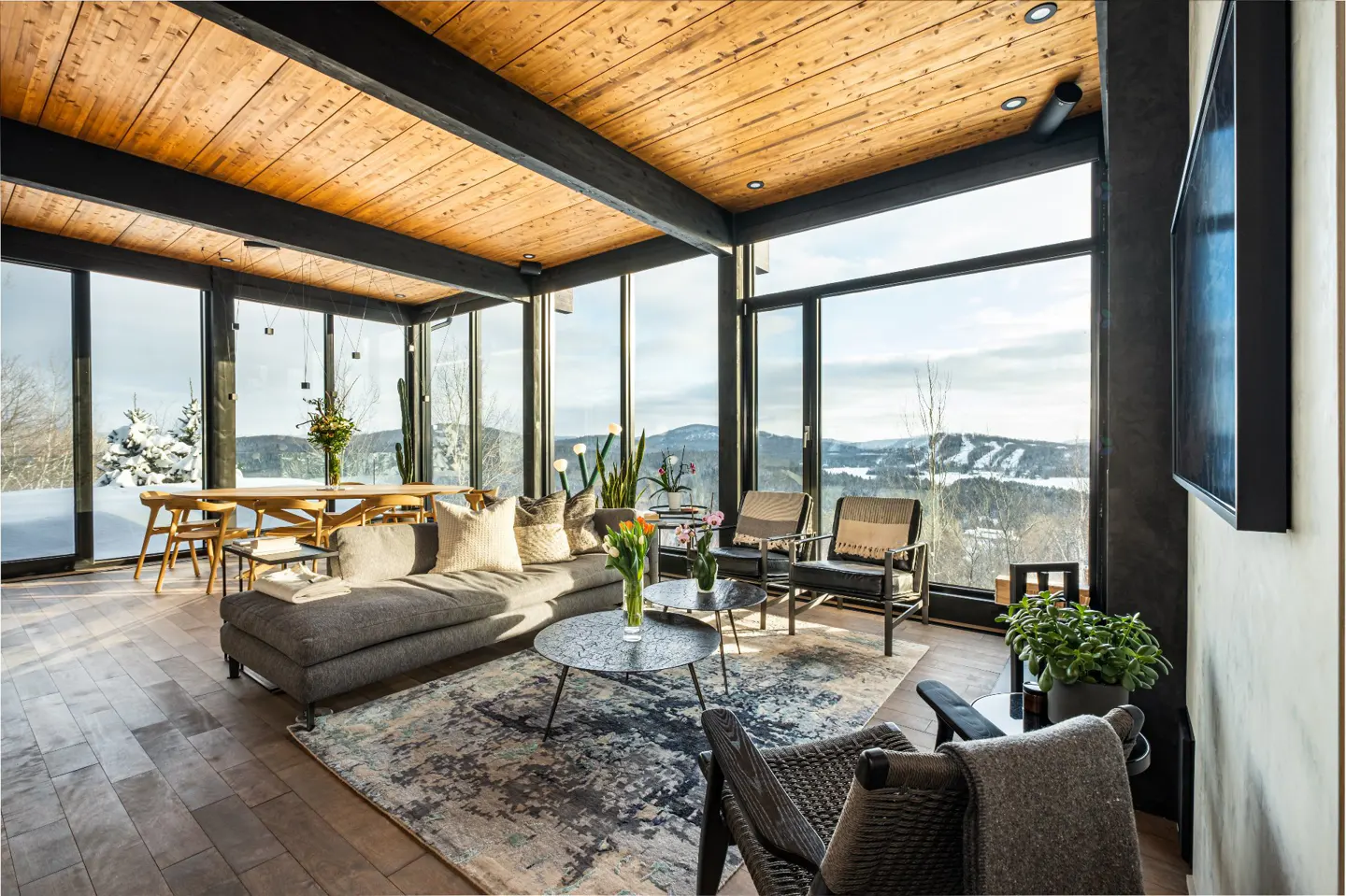 Modern living room with wood ceiling, floor-to-ceiling windows, gray sofa, area rug, and mountain view.