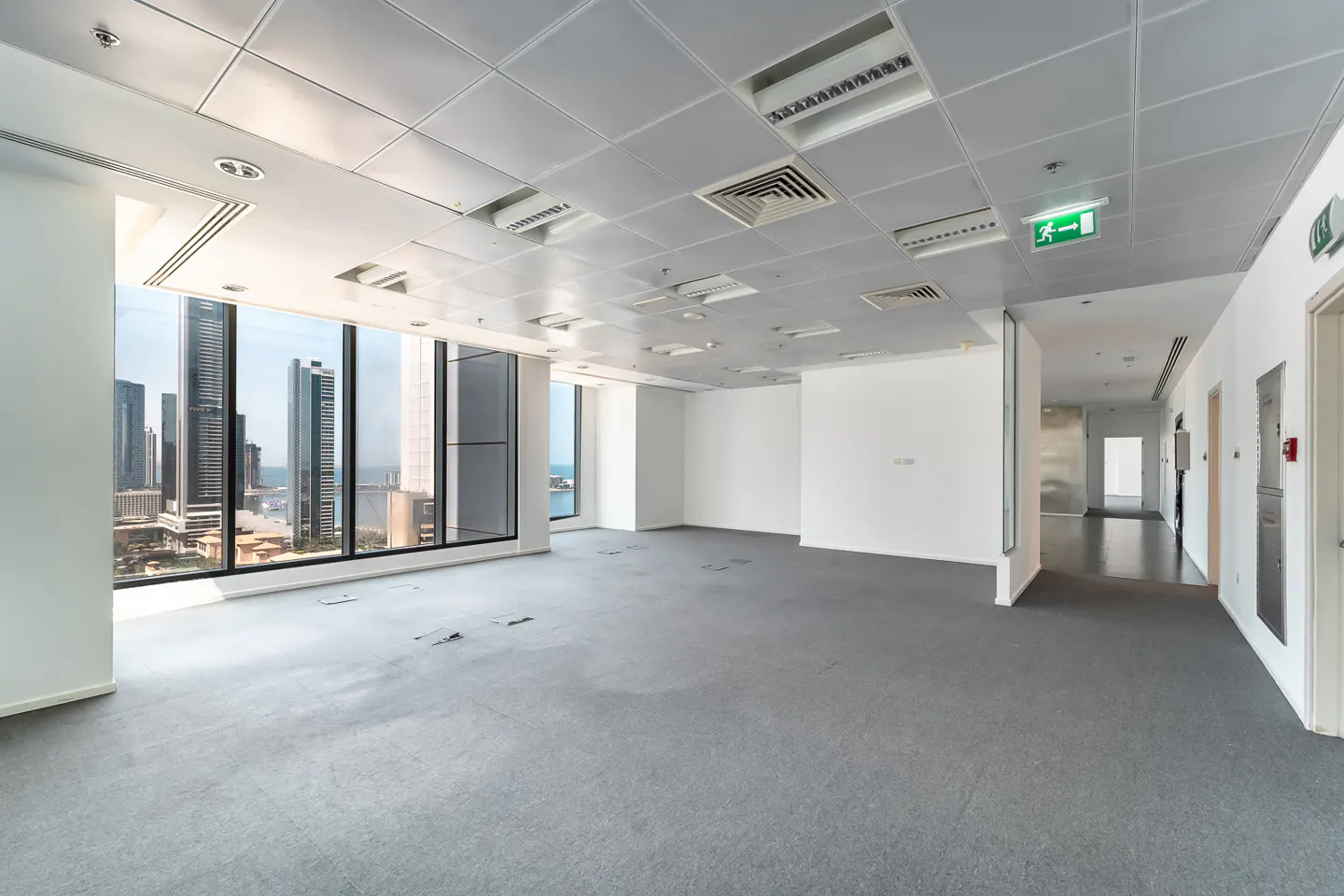 Bright, empty office space with gray carpet, white walls, and large windows overlooking a city skyline.