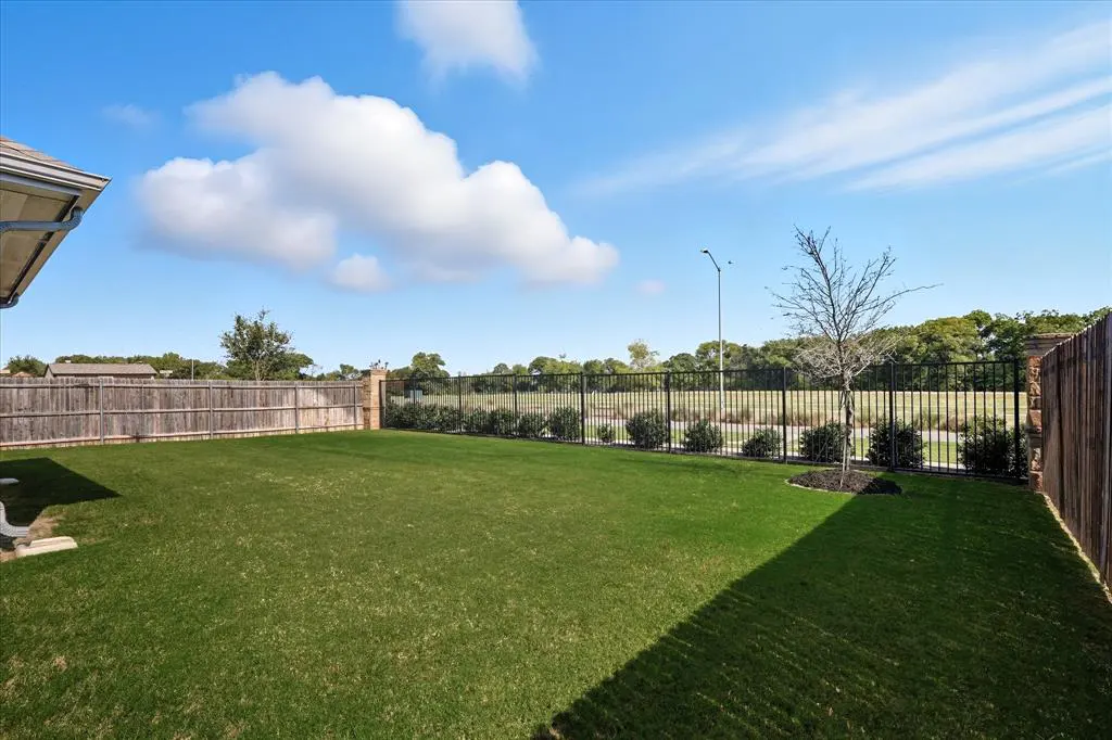 A large, green lawn is enclosed by wood and iron fences under a blue sky with white clouds.