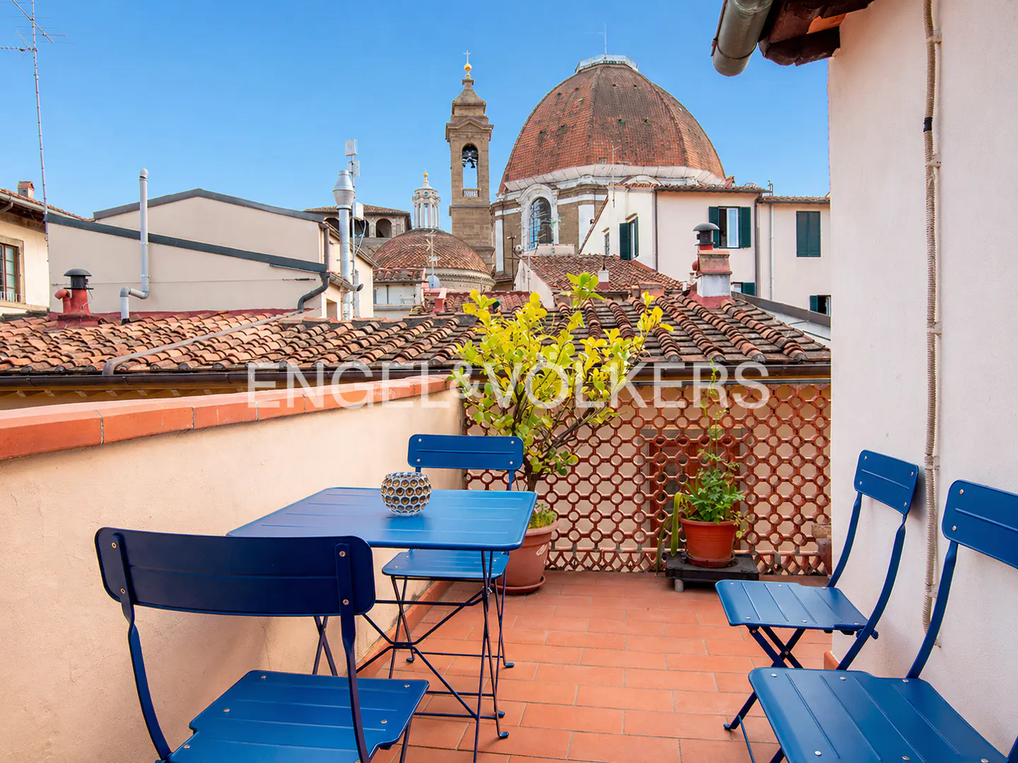 Rooftop terrace with blue table and chairs, overlooking terracotta rooftops and the dome of a church in Florence, Italy.