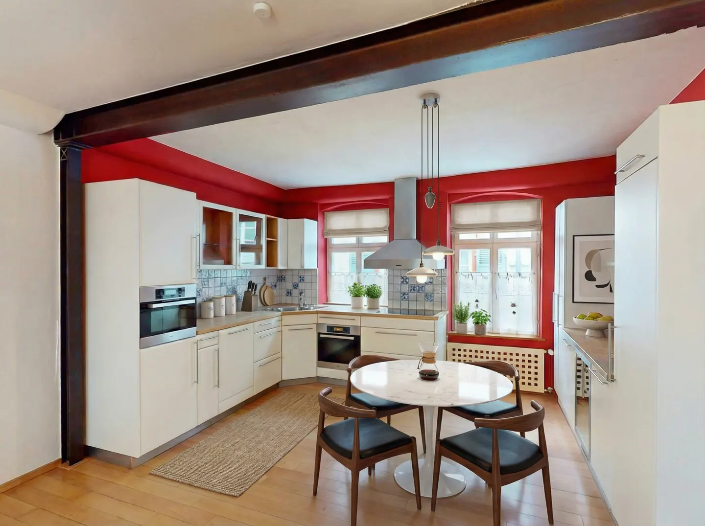 A modern kitchen with white cabinets, red walls, and a round marble table with four chairs.