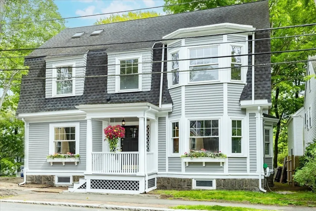 Exterior view of a two-story gray house with a dark roof, white trim, and a front porch with hanging flowers.