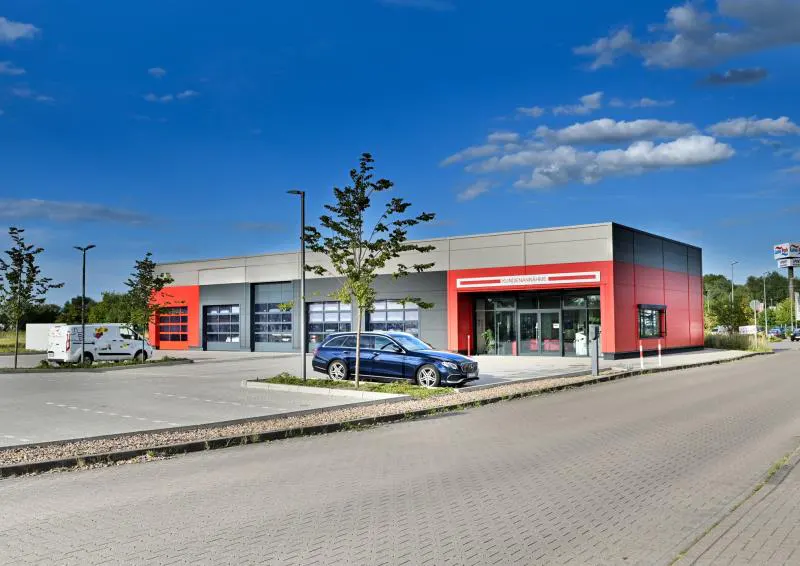 Exterior of a modern, gray and red commercial building with a blue car parked in front.