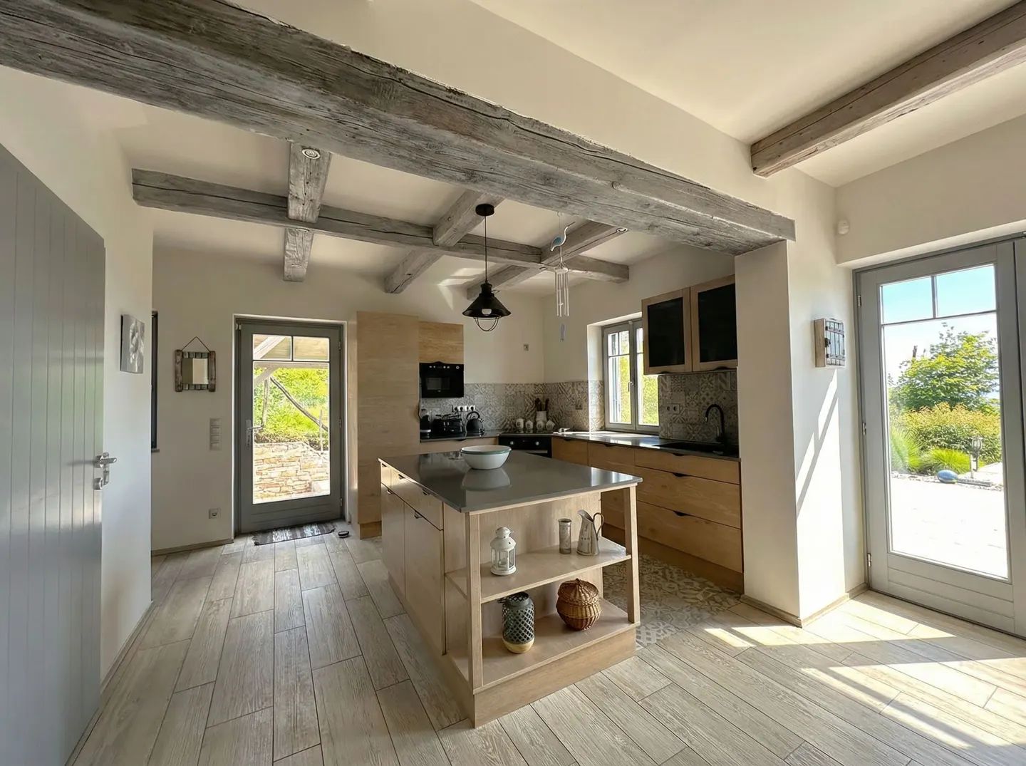 Bright kitchen with wood floors, island, and exposed beams. Natural light streams in from the doors and windows.