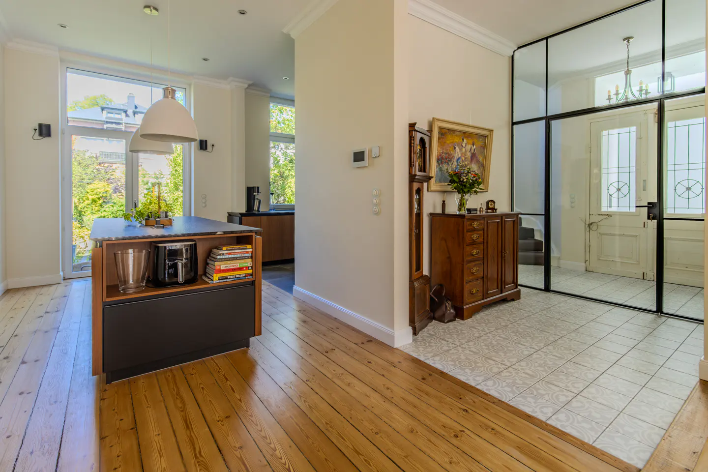 Modern kitchen with island and wooden floors, leading to a tiled entryway with a wooden cabinet and glass-paned front door.