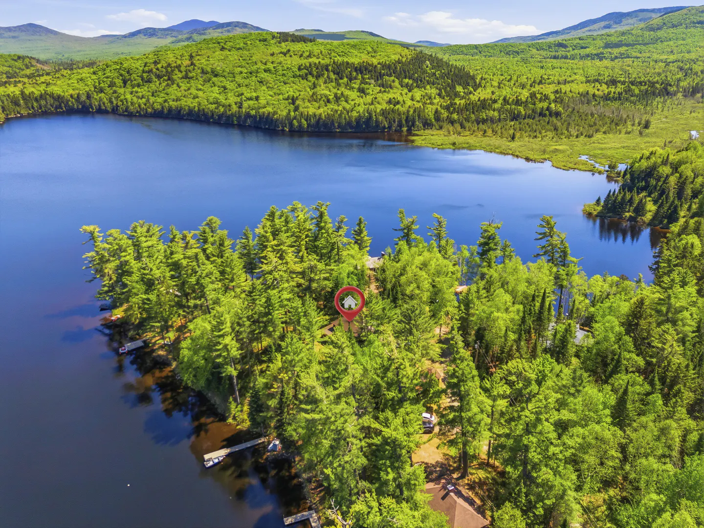 Aerial view of a house nestled in a lush green forest by a blue lake, marked by a red location pin.