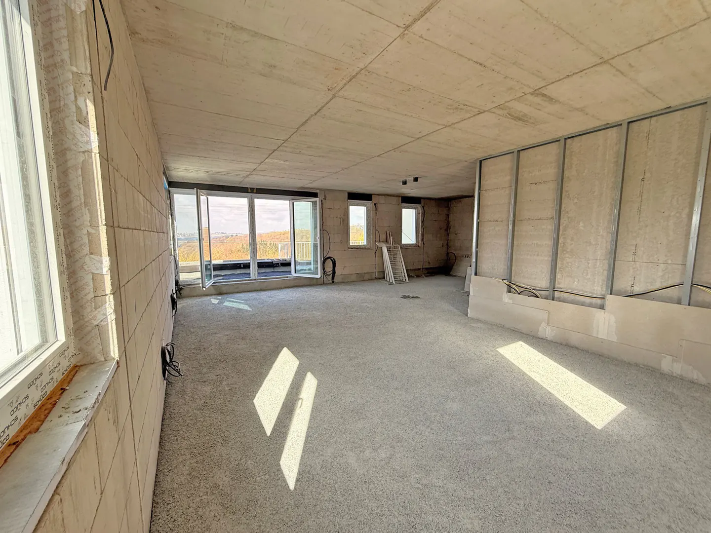 Unfinished room with concrete walls, floor, and ceiling. Large windows and sliding glass doors offer a view of the landscape. Metal framing on one wall.