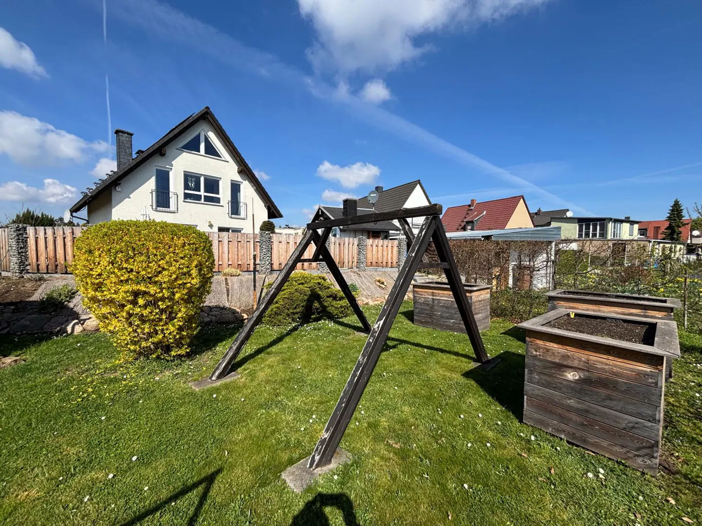 A backyard with a swing set and raised garden beds on a sunny day. A house is visible in the background.