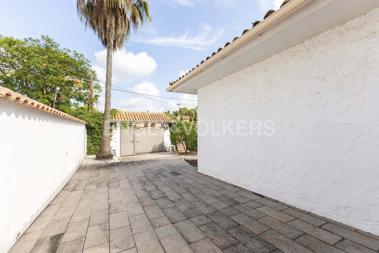 Exterior view of a white stucco house with a gray stone driveway and a palm tree.