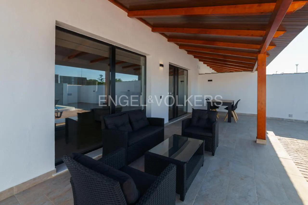 Outdoor patio with black wicker furniture, glass table, and wooden pergola. Sliding glass doors lead inside. Engel & Völkers logo visible.