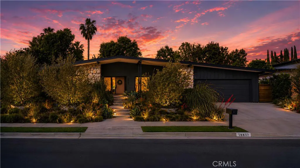 A modern single-story home with stone accents, dark gray siding, and a matching garage door under a vibrant sunset sky.