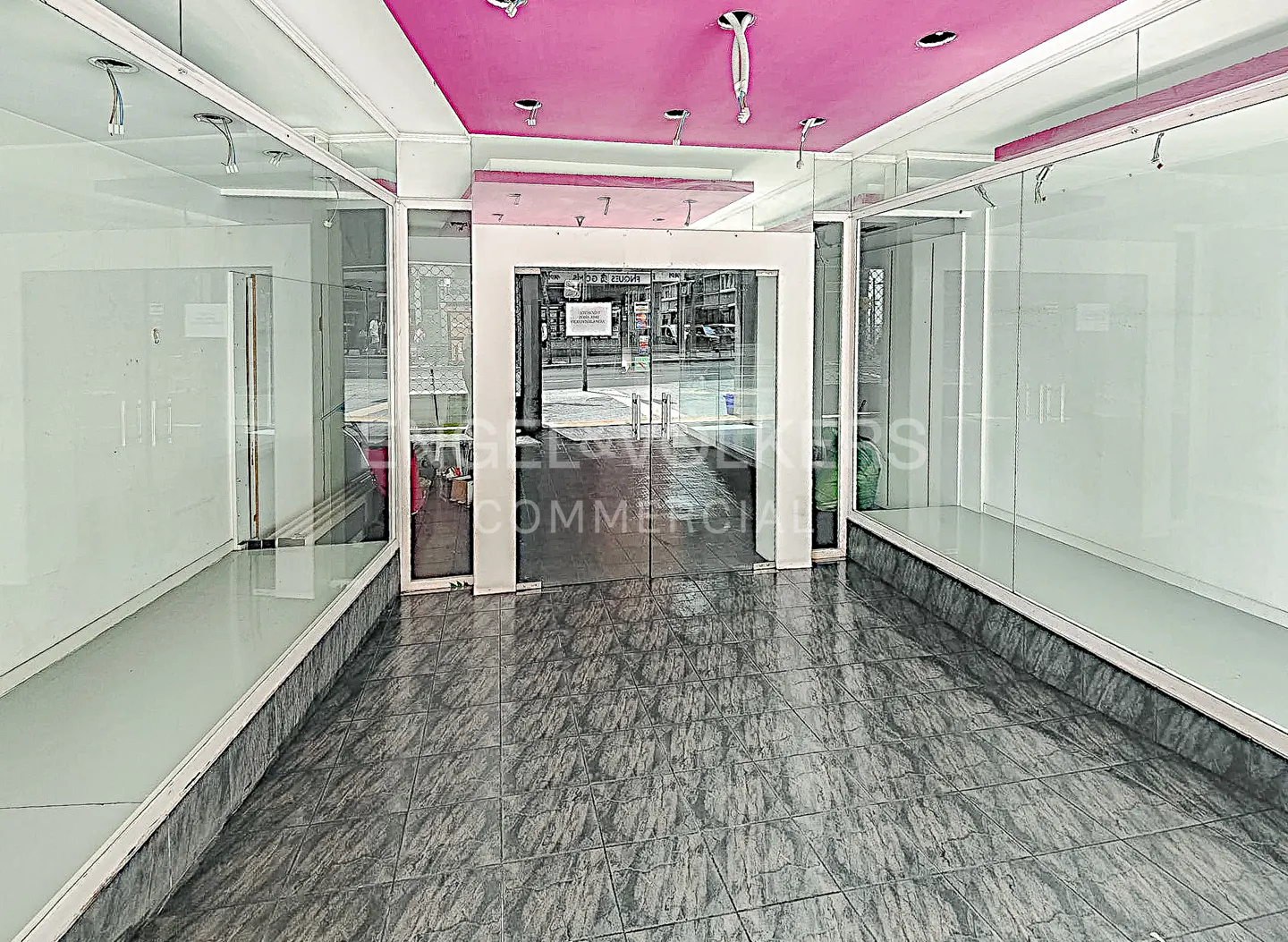 Empty commercial space with glass storefront, gray tile floor, and pink ceiling.