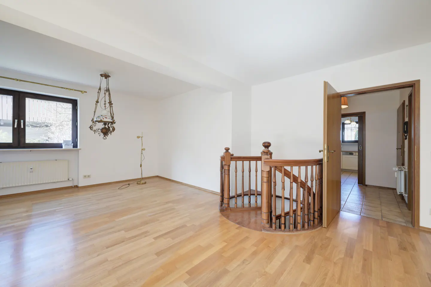 Bright, empty room with wood floors, white walls, and a spiral staircase. A window and doorway are visible.