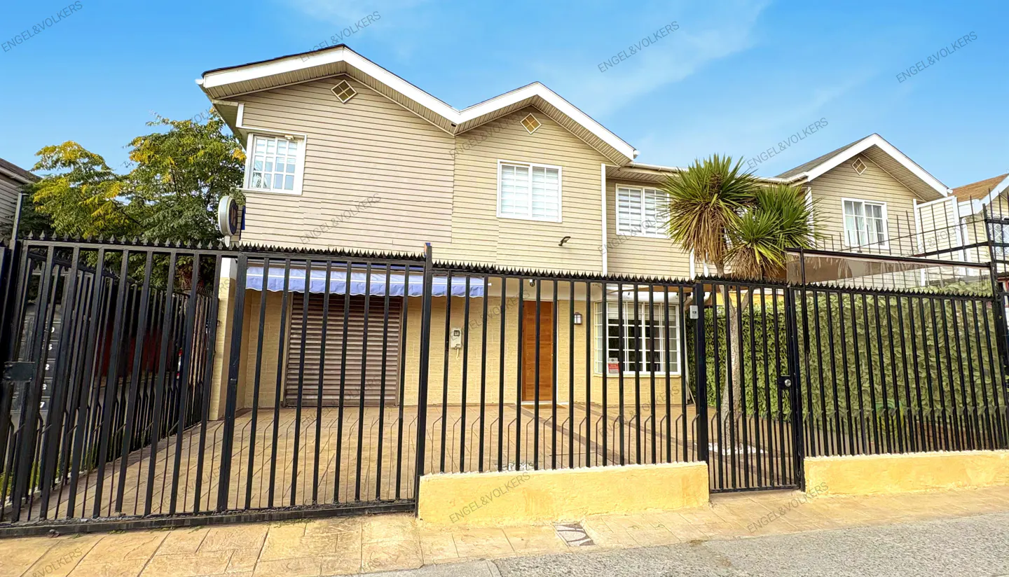 Two-story beige house with a black iron fence, a brown door, and a blue awning under a bright blue sky.