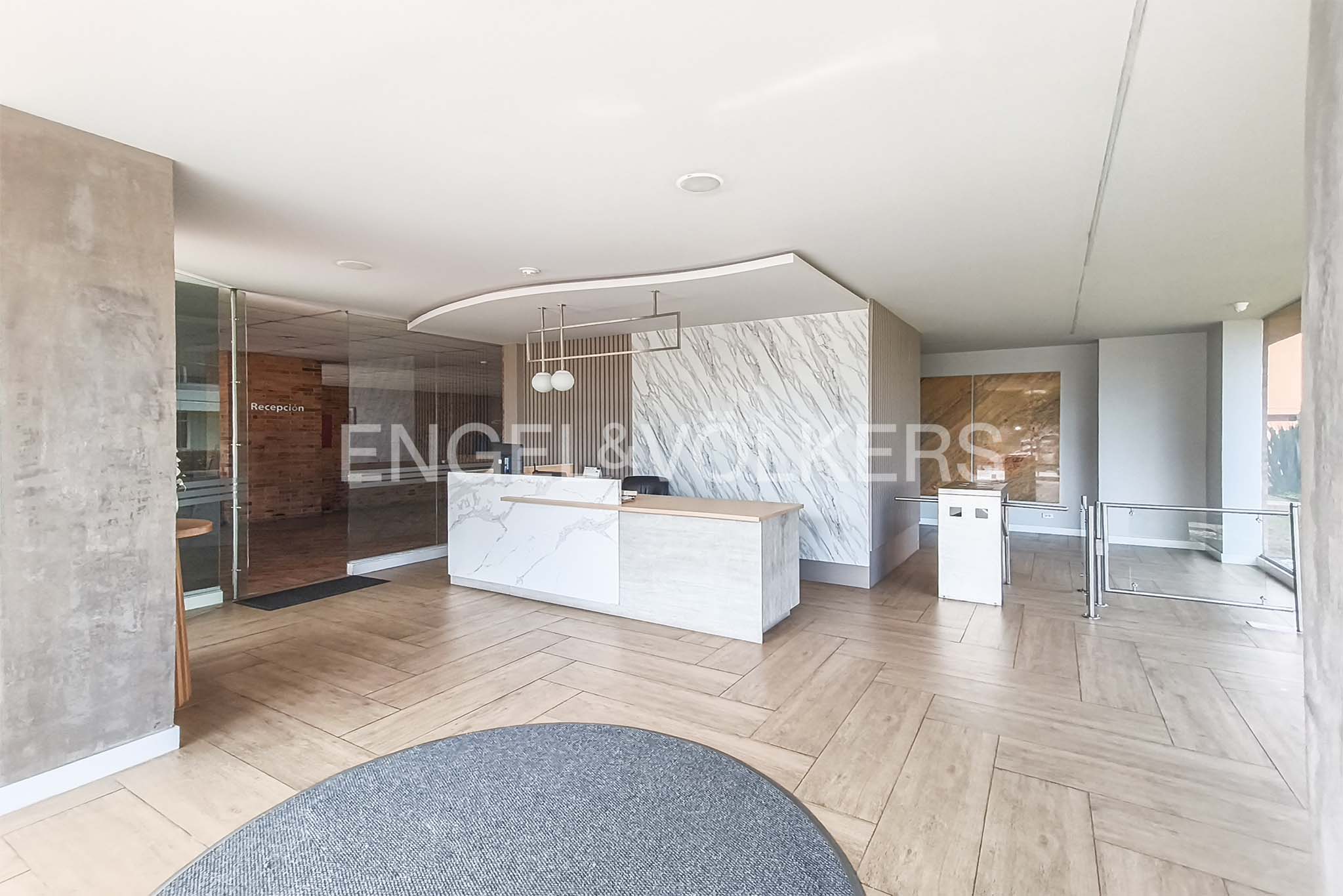 Modern office lobby with a white marble reception desk, wood-look tile floors, and a glass-enclosed entrance area.