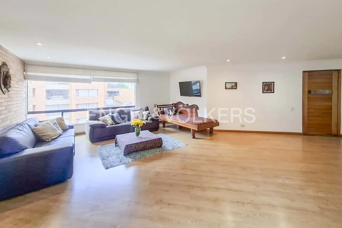Bright living room with hardwood floors, blue sofas, a chaise lounge, and a large window.