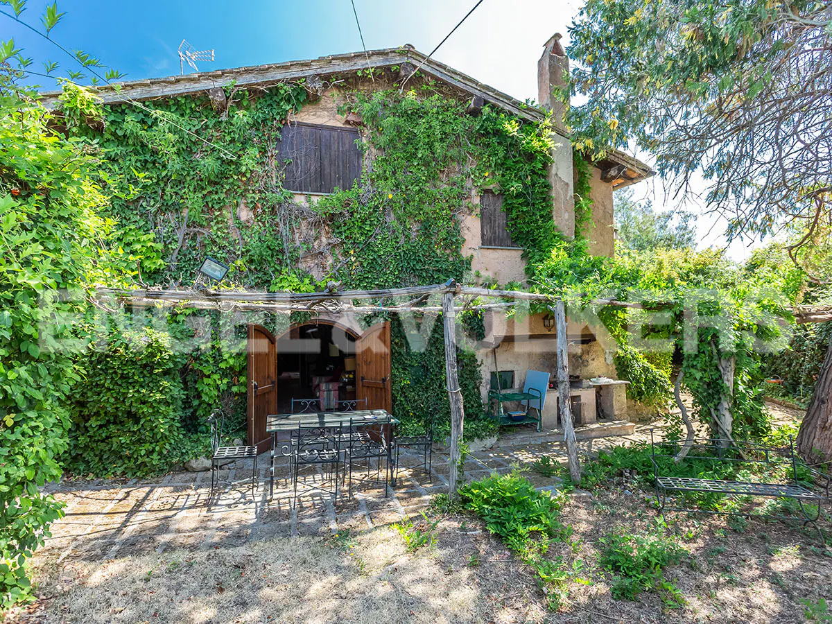 Exterior view of a two-story house covered in green vines, with a patio table and chairs in front.