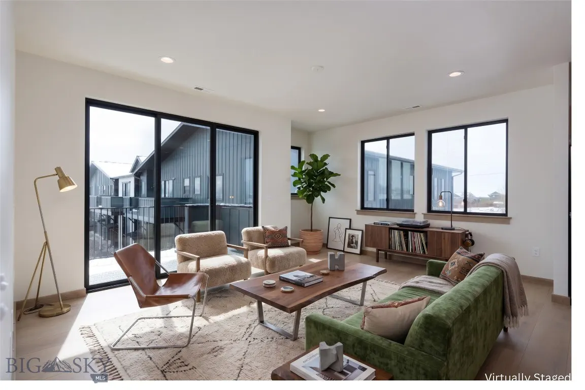 Bright living room with a green sofa, two beige chairs, a brown leather chair, and a wooden coffee table on a patterned rug.