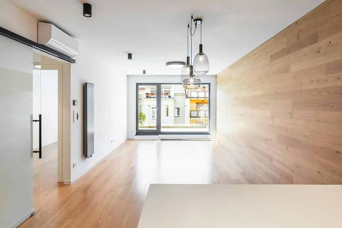 Modern living room with light wood flooring, a wood-paneled wall, glass door, and three hanging pendant lights.