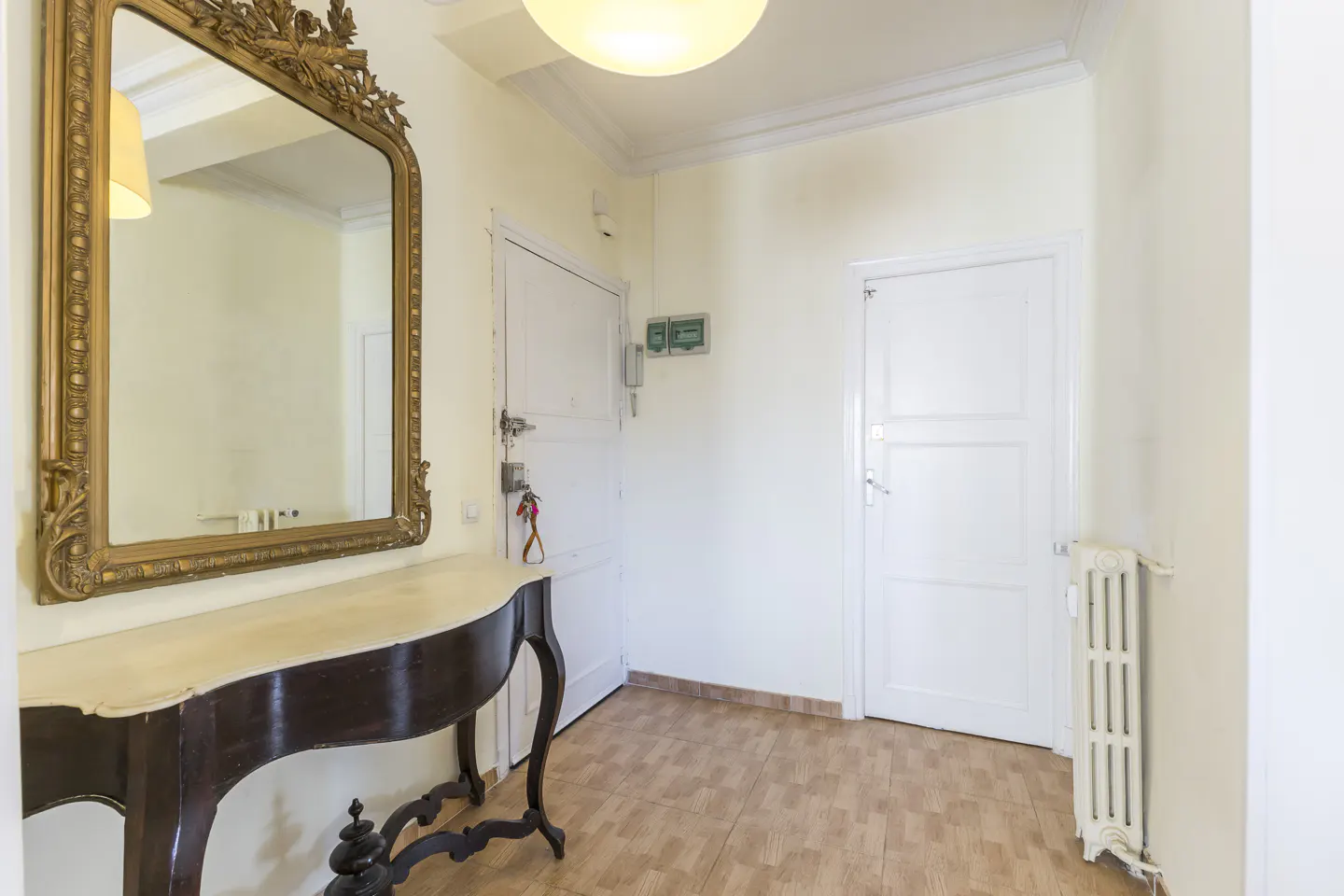 Entryway with a dark wood console table, marble top, and ornate gold mirror. Two white doors and a radiator are visible.