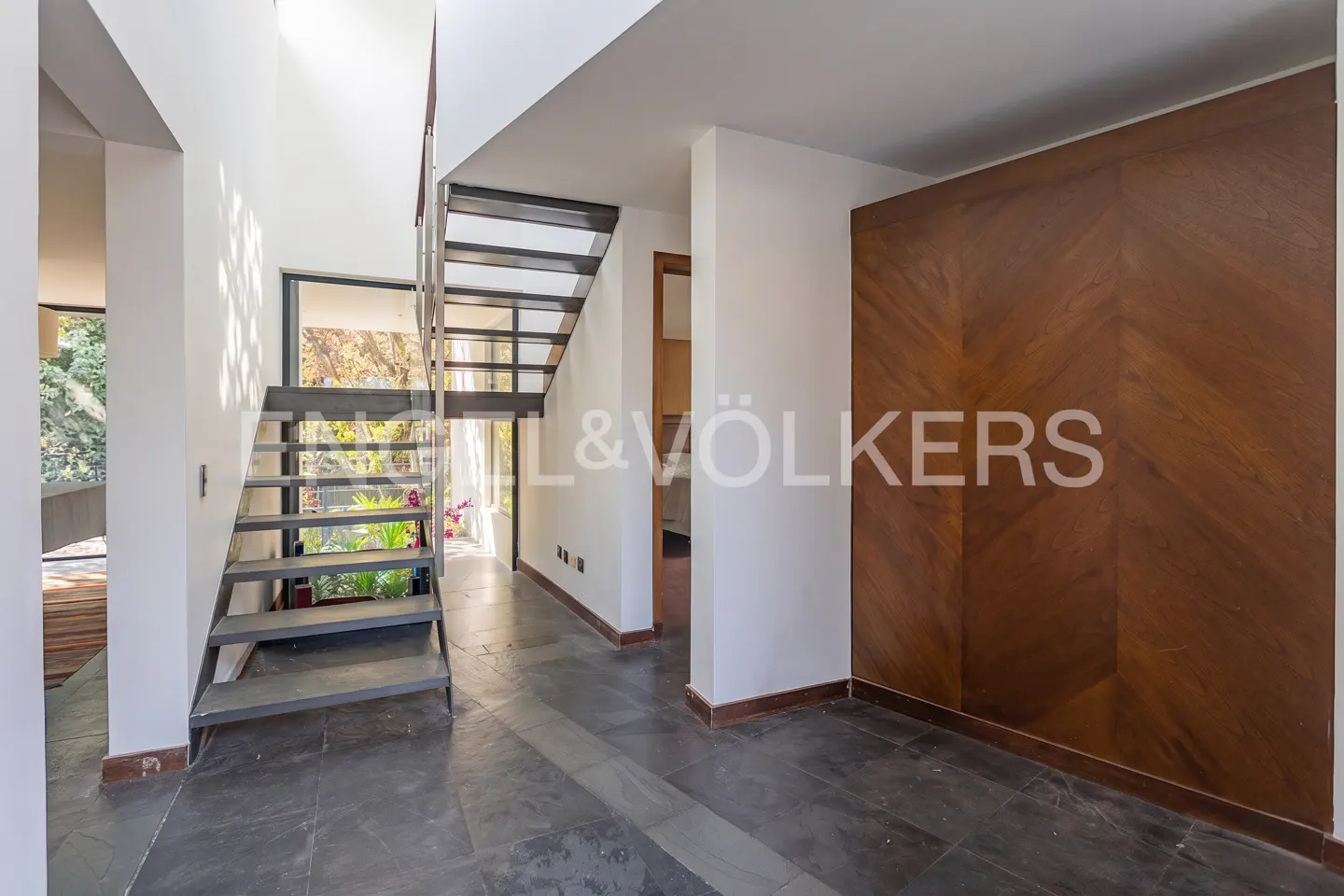 Modern foyer with dark slate floors, a floating metal staircase, and a large chevron-patterned wood accent wall.