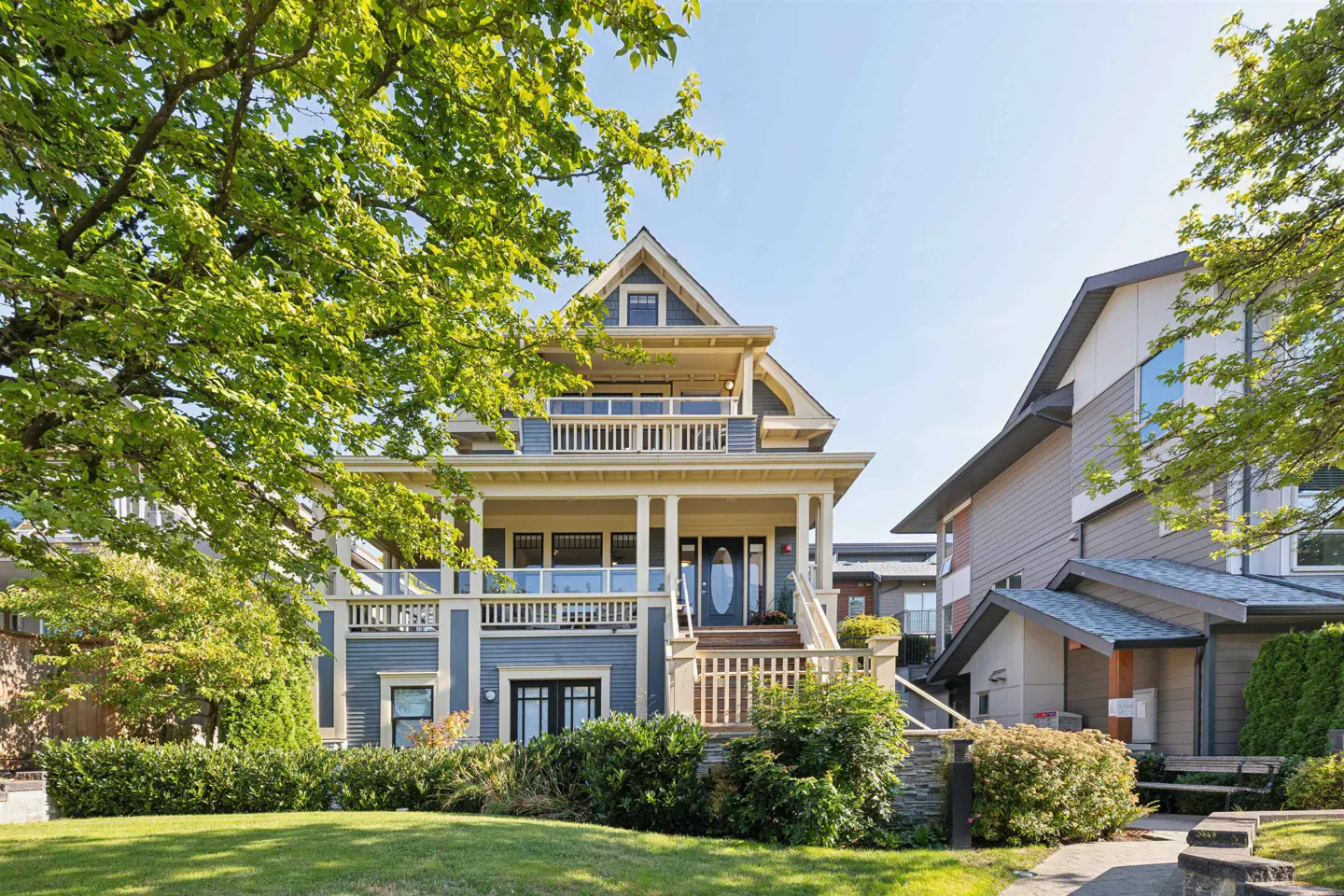 Two-story blue house with white trim, a porch, and a balcony, surrounded by green trees and grass.