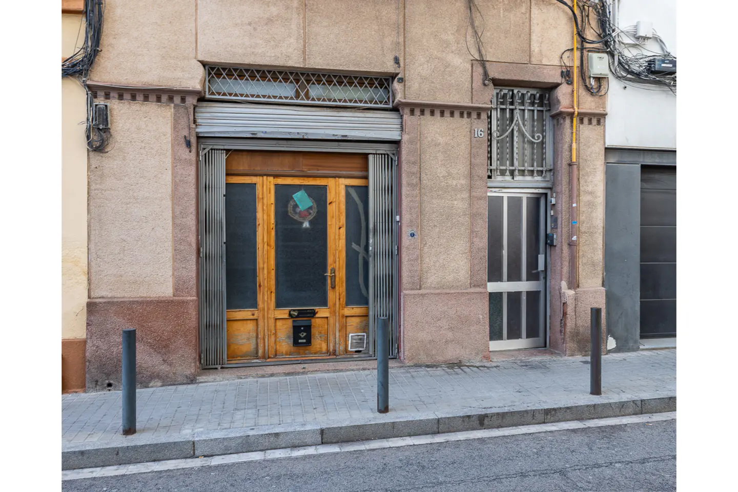 Exterior view of a building with a wooden door and metal security gate, next to a metal door with bars on the window.