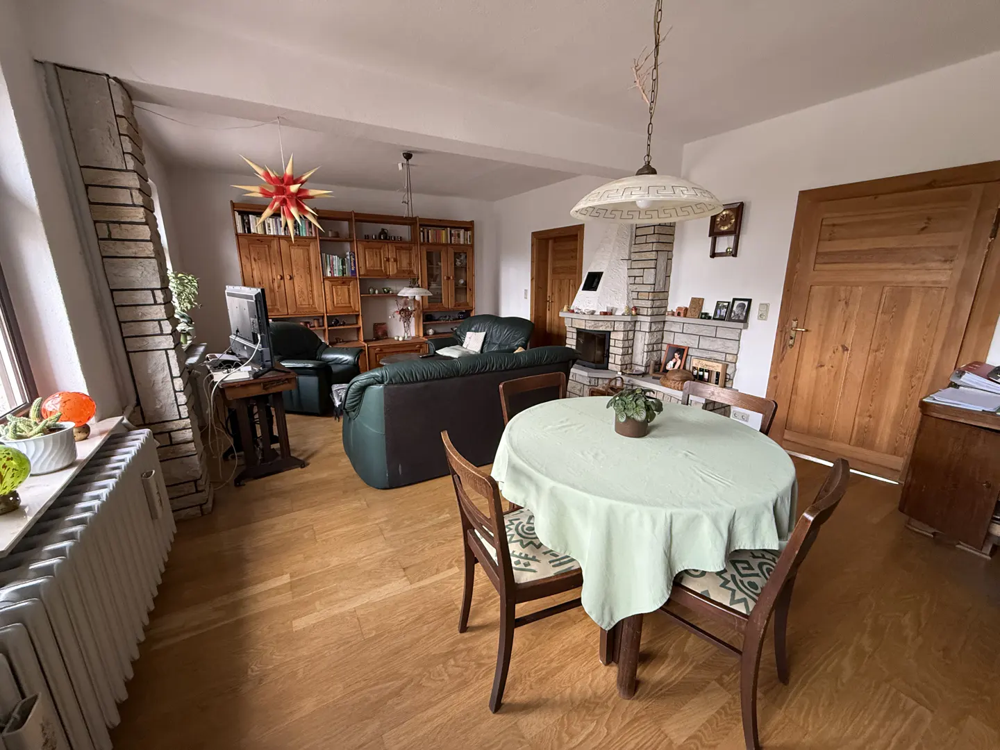 A living room with a round table covered with a light green tablecloth, wooden chairs, a green leather sofa, and a stone fireplace.