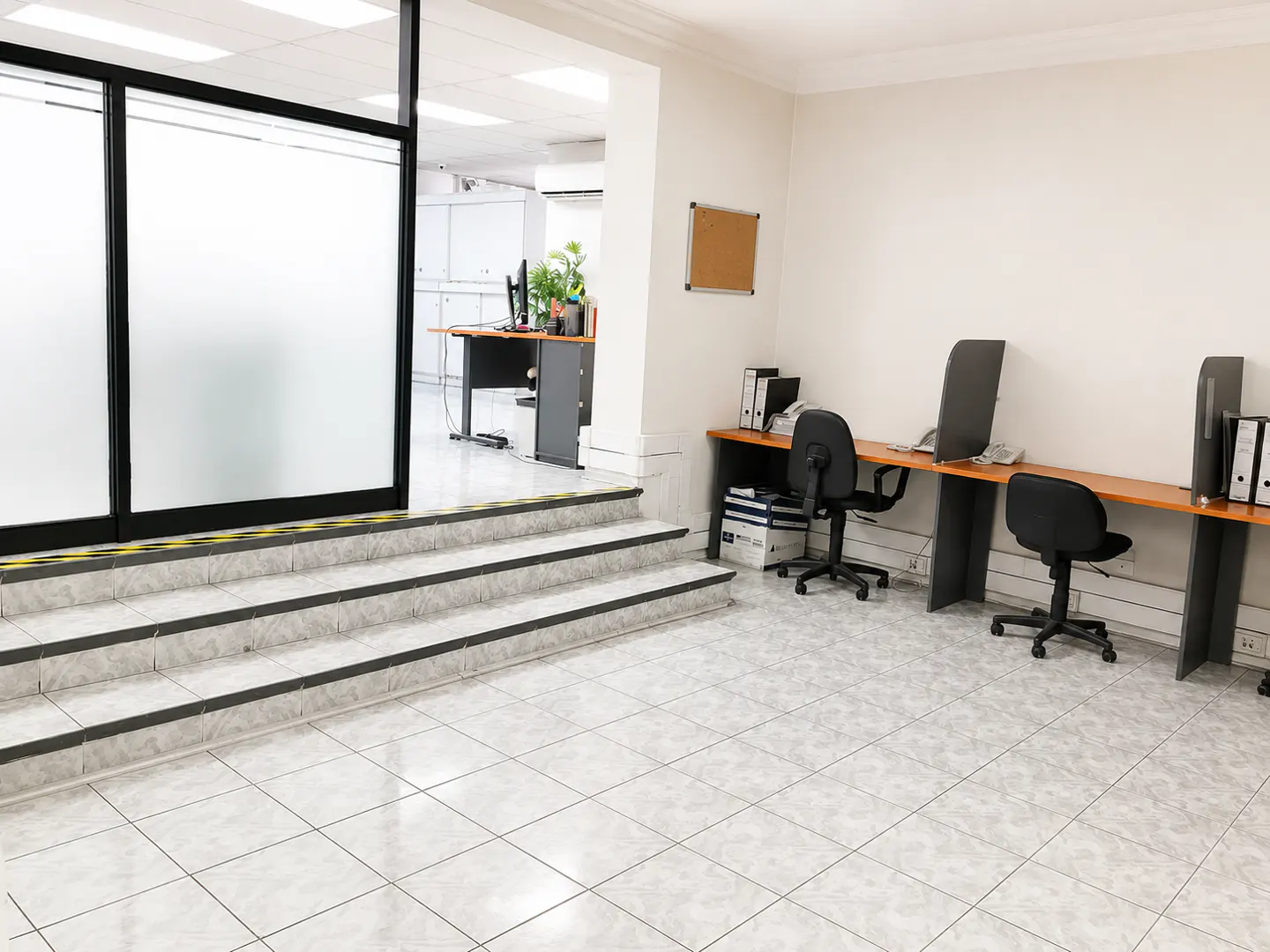 Modern office space with tiled floors, a three-step entry, and two workstations with black chairs and wooden desks.