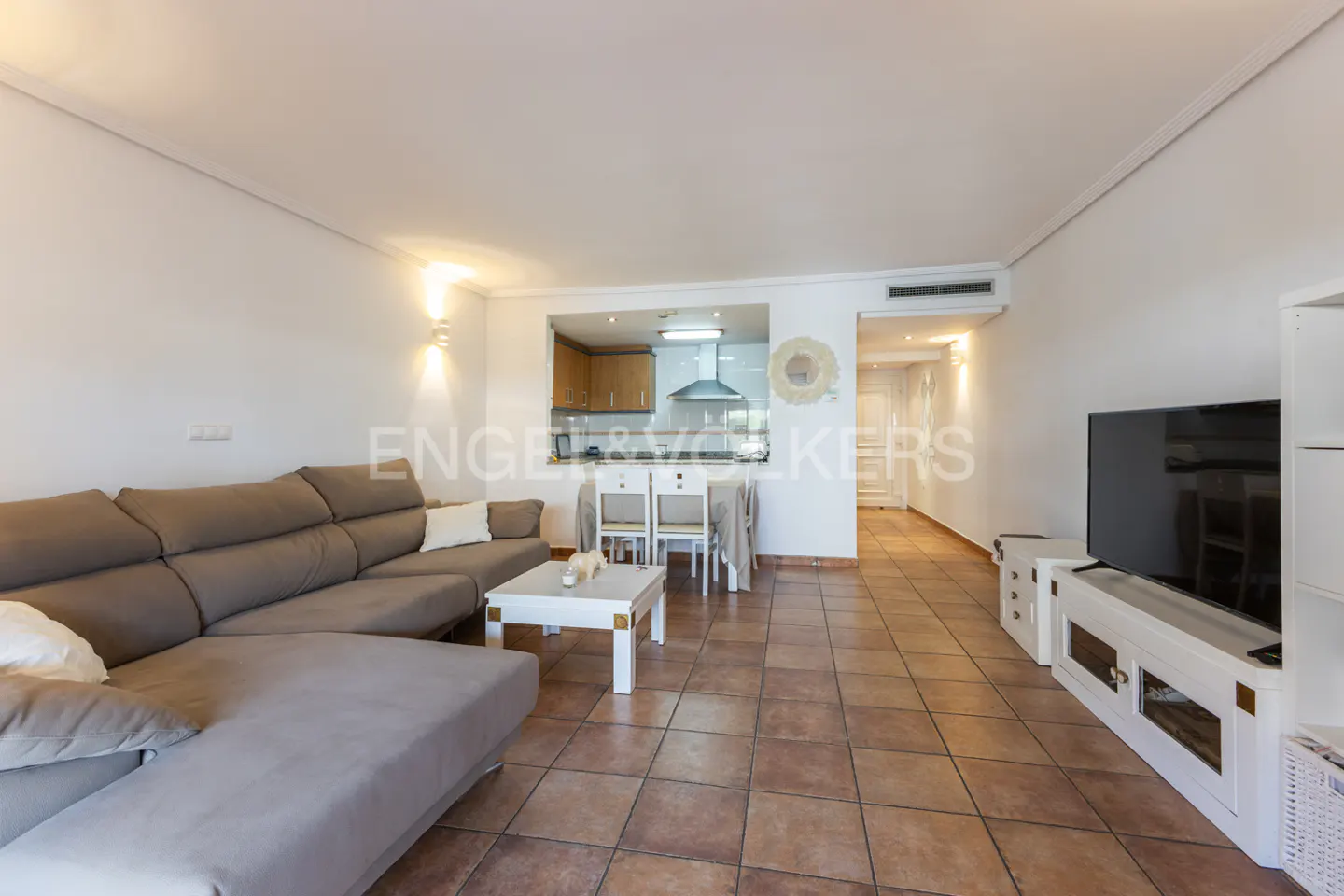 Open-concept living room with a brown sectional sofa, white coffee table, and a view into the kitchen with a dining table.