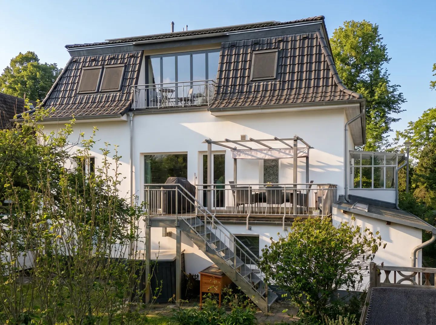 Exterior view of a white two-story house with a brown tiled roof, balconies, and a metal staircase.