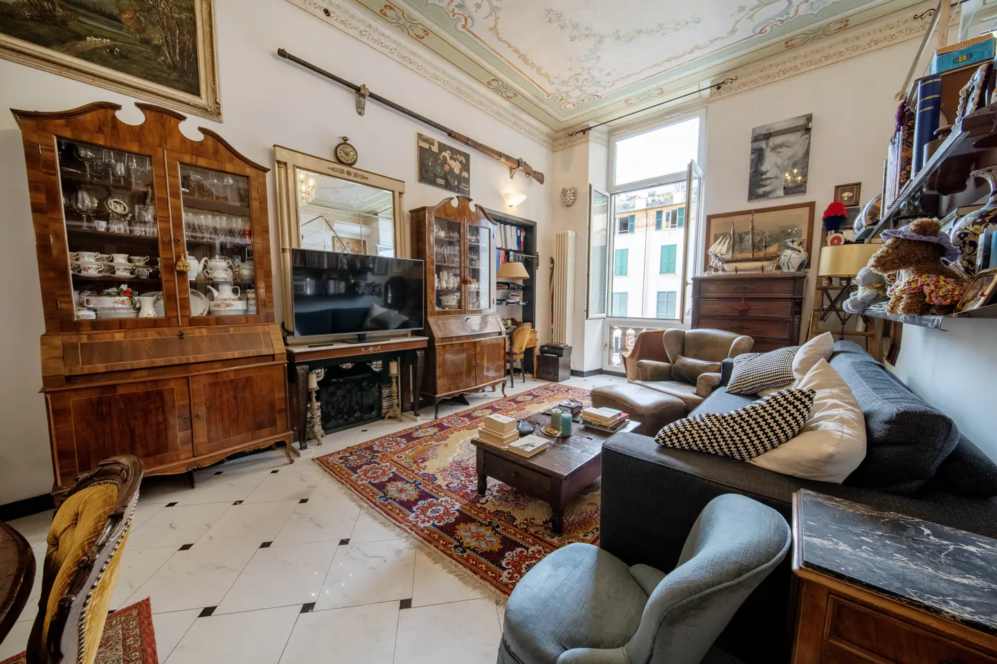 A living room with antique furniture, a patterned rug, and a view from the window.