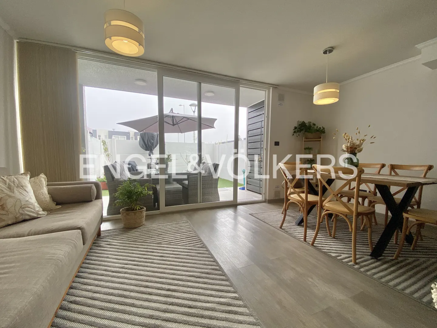 A bright living room with a beige sofa, a dining table with wooden chairs, and a patio view.