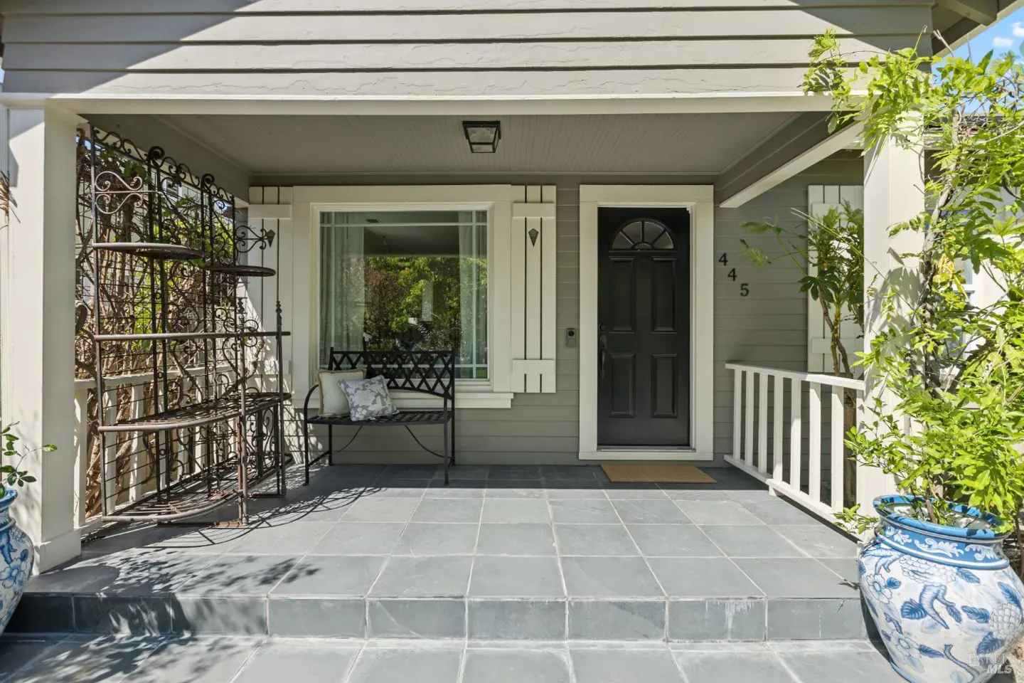 Front porch of a gray house with a black door, bench, and potted plants.