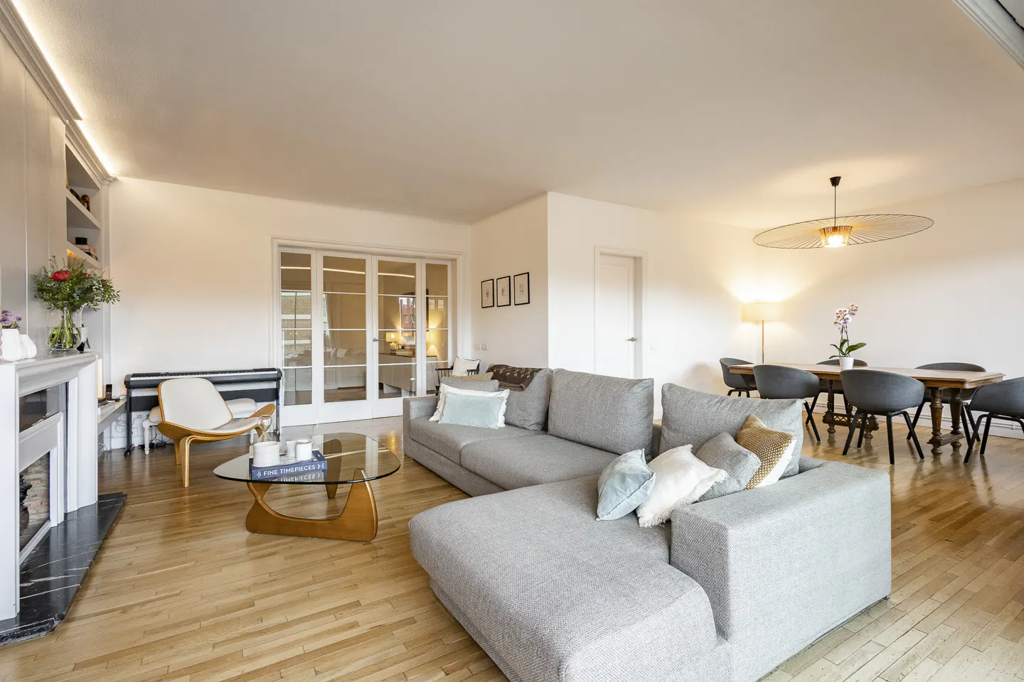 Bright living room with hardwood floors, a gray sectional sofa, a glass coffee table, and a dining table with chairs.