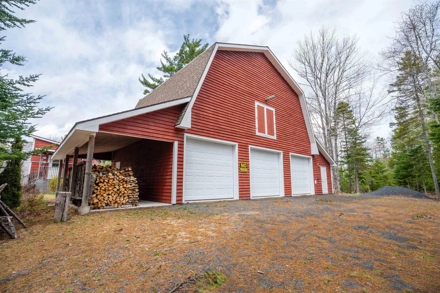 Red barn-style garage with three white doors and a wood storage area on a grassy lot.